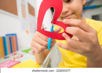 Girl cutting out paper heart, selective focus