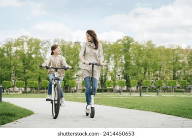 Girl cycling while mother riding electric scooter in city park - Powered by Shutterstock