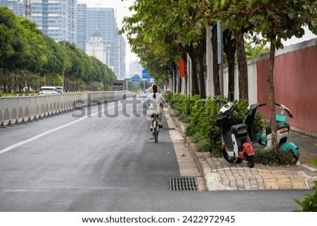 Girl cyclist in a dress with her back to the road, young joyful carefree woman riding fast along the street, arrow in the direction, chamomile flowers, urban background, China