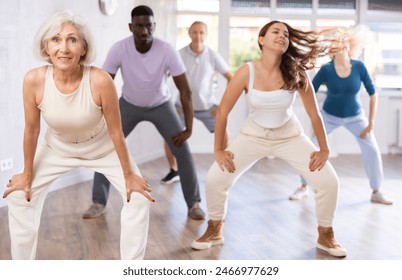 Girl dance teacher instruct group of elderly people to dance modern dances. Young woman moves freely and dance hip-hop with unfastened hair in fitness studio - Powered by Shutterstock