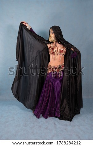 A girl a dancer an animator in a black Cape a cloak with a veiled face on a blue background waved her hand with the black cloak's flaps like a mysterious image