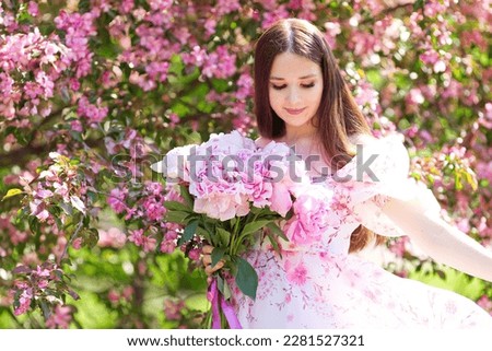 A girl dancing with a bouquet of pink peonies in a blooming garden