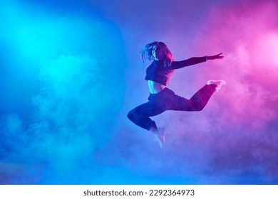 a girl in dark clothes dances on a neon background in smoke, modern dance - Powered by Shutterstock