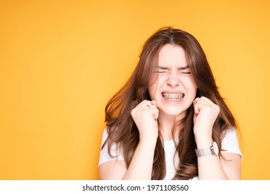 Girl with dark hair with braces clenching her teeth due to pain in the jaw closing her eyes and clenching her hands into fists