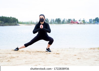 A Girl With Dark Hair And Fair Skin In Black Sportswear And A Black Protective Mask Is Engaged In Sports On The Sand By The Lake In The Forest.