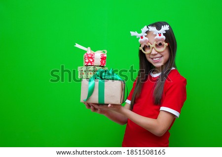 A girl with dark hair in a red T-shirt and in funny glasses in her hands holds boxes of gifts for the Christmas holidays and New Year.