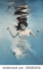        A girl with dark hair in a white dress swims underwater as if flying in zero gravity                       