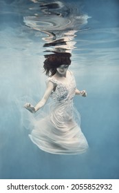        A girl with dark hair in a white dress swims underwater as if flying in zero gravity                       
