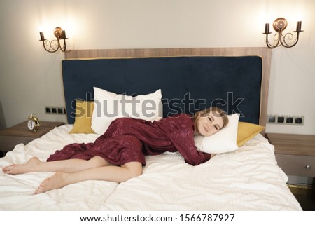 Girl in dark red bathrobe relax on the bed in her bedroom alone and cheerful