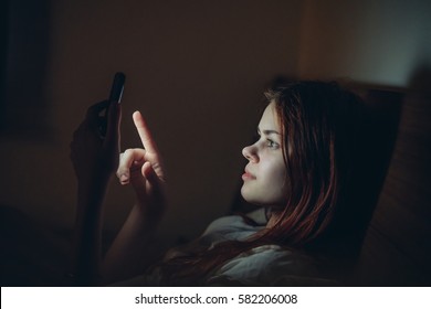 Girl In A Dark Room On The Bed With The Phone.