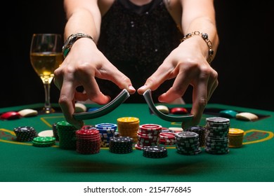 A girl dealer or croupier shuffles poker cards in a casino on the background of a table, chips, and a glass of wine. The concept of poker game, gaming business
