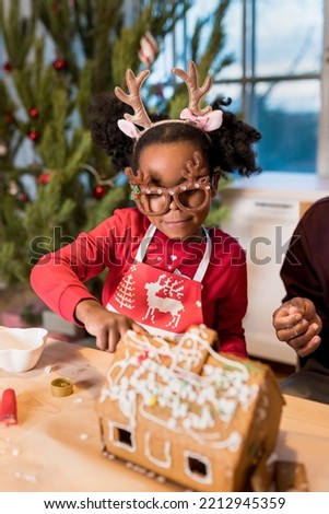 Girl decorating gingerbread house. Kids assembling tasting gingerbread cookies for Christmas holidays. Happy moments at home concept