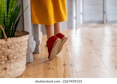 Girl in deep yellow dress is standing on tiptoe by wooden cupboard in the kitchen. Close-up burgundy childs shoes standing on light laminate floor. In handmade rustic planter green flower sansevieria - Powered by Shutterstock