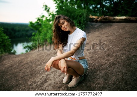A girl in a delicate blue dress walks along a path on the top of a mountain near the river