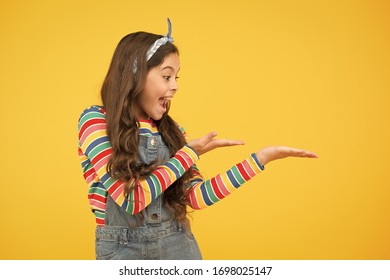 Girl Demonstrate Product. Promoting Product For Kids. Launching Product. Advertisement Concept. Product Presentation. Kid Happy Smiling Face Show Something On Open Palm Copy Space Yellow Background.