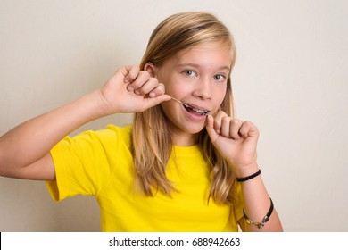 Girl With Dental Braces Flossing Teeth. Close-up Portrait Of Pre Teen Girl With Dental Floss Isolated.