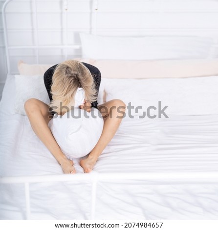 The girl in depression sits on the bed. The girl is enjoying the evening in an embrace with a pillow on the bed. Girl mood concept