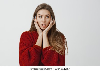 Girl Did Not Know What To Do After Shocking Revelation. Indoor Shot Of Worried Attractive Caucasian Woman In Stylish Red Sweater, Holding Palms On Face And Looking Aside With Troubled, Confused Face