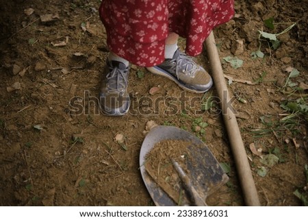 A girl in dirty sneakers stands near a shovel after working in the garden