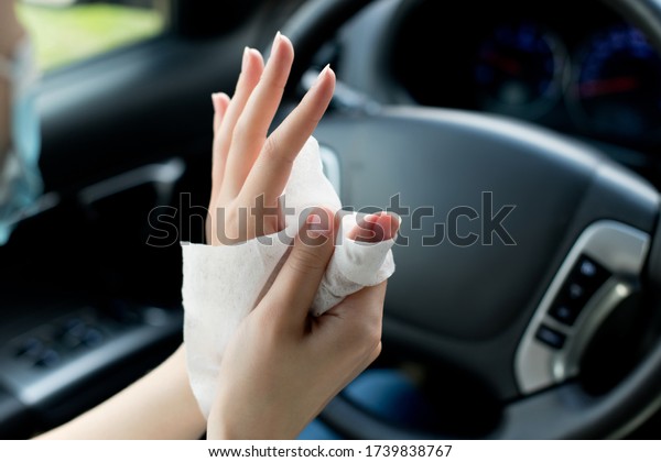 girl disinfects hands with an\
antiseptic napkin on the background of a car steering\
wheel