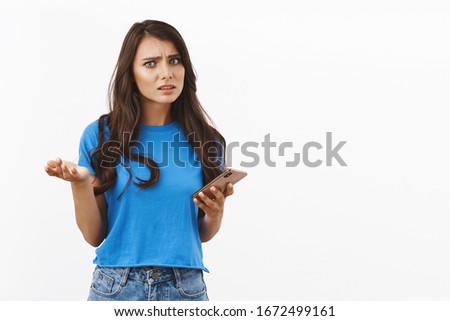 Girl disturbed with strange creepy message. Problematic, concerned brunette woman holding smartphone, shrug and raise hand puzzled, frowning questioned, looking camera confused