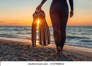 A Girl Diver In A Wet Suit Holds Flippers In Her Hands.