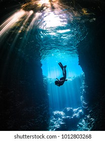 Girl diving in cavern with lightbeams coming on top of her - Shutterstock ID 1012803268