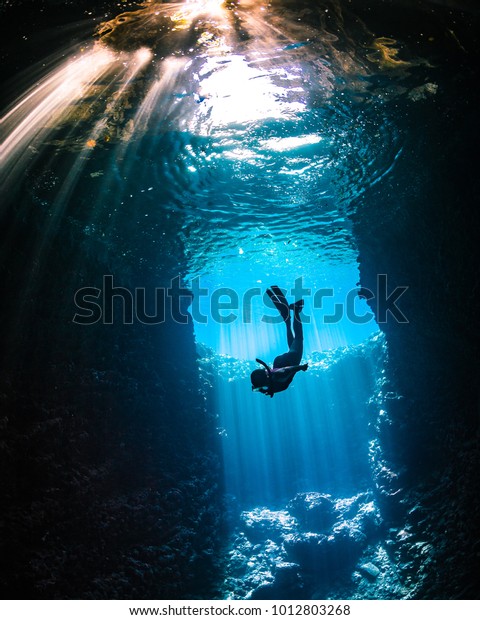 Girl diving in cavern with lightbeams coming on top\
of her