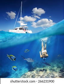 Girl diving in ocean with fishes next to catamaran at sunny day.