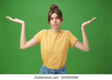 Girl Do Not Know Anything. Portrait Of Confused Unsure Cute Woman With Combed Hair Shrugging With Raised Hands Pouting Looking Clueless At Camera Standing Questioned Against Green Background