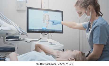 Girl doctor dentist demonstrates a 3D model of teeth on a touch monitor, rotates her hands. Dental consultation in the clinic, diagnostics. Jaw scan, digital imprint, medical digital technology. - Powered by Shutterstock