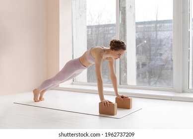 Girl does yoga. Young woman practices asanas near large bright window. Pilates block yoga cork brick. - Powered by Shutterstock