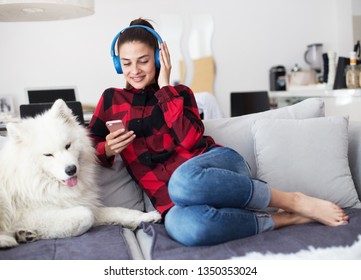Girl with a dog listening to music. Woman with a dog at home using headphones.