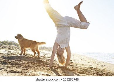 Girl with dog on the beach, doing cartwheels with the sun filtering through.