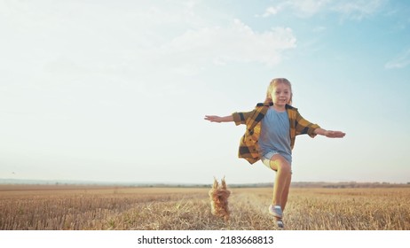 Girl And Dog Running. People In The Park. Little Girl Child Running Across A Mowed Wheat Field With A Pet Dog Happy Smiling. Happy Family Kid Concept. Child Girl Run The Park With Dream A Dog