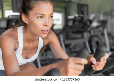 Girl Doing Cardio Class At Gym On Exercise Bike. Indoor Cycling With Wheels Spinning. Focus And Weight Loss Motivation. Young Mixed Race Asian Caucasian Woman Training Fitness Workout On Bicycle.