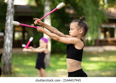 Girl doing exercise with clubs on rhythmic gymnastics training with other trainees outdoors in summer in sports camp