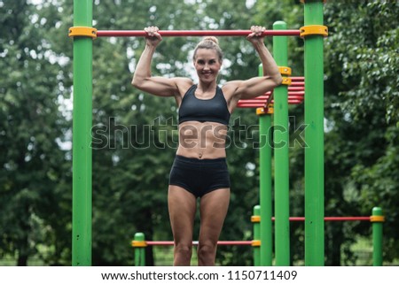 girl doing exercises on the horizontal bar in the open air. The woman is engaged in workout