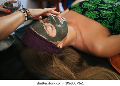 The Girl Doing The Facial Massage. The Girl Put A Clay Mask On The Face. The Cream On The Face. Ayurvedic Treatment. Spa Treatments In Asia. Ayurveda Salon
