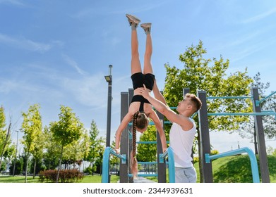 Girl doing hand stand push ups exercise in parallel bars. Personal trainer helps a girl to hold a handstand on the uneven bars. - Powered by Shutterstock