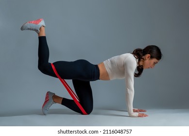 Girl doing kneeling hip extension with resistance band on grey background