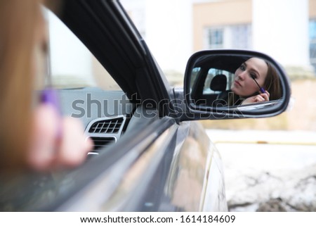 Girl doing makeup looking in the rear view mirror in the car
