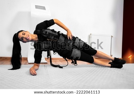 Girl doing side plank attached to ems machine and smiling 