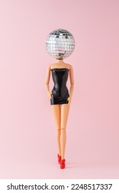 Girl doll in black dress with disco ball head on pink background. Minimal party concept.