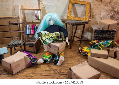 Girl doll with green hair sitting on the floor unpacking clothes from cardboard boxes in a messy attic filled with junk. 