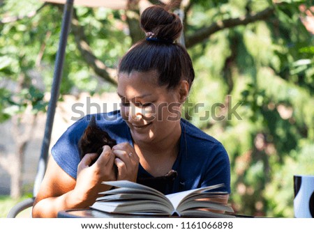 Girl with domestic black cat reading book in backyard