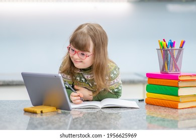 A girl with down syndrome is engaged in lessons using a tablet. Child down smiling while looking at the computer during class. Accessibility of education for children with disabilities 