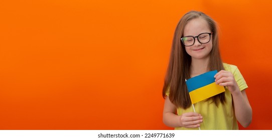 A girl with Down syndrome holds the flag of Ukraine. orange background. Banner - Shutterstock ID 2249771639