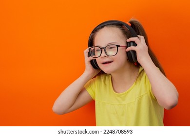 Girl with Down syndrome listens to music. Orange background - Shutterstock ID 2248708593