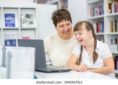 Ein Mädchen mit Down-Syndrom benutzt einen Laptop mit ihrem Lehrer in der Bibliothek. Konzept "Bildung für behinderte Kinder"